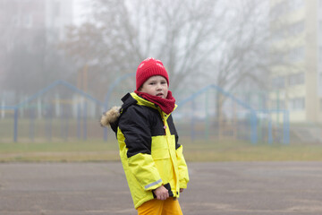 A little boy in a yellow jacket lost in the fog in the city.