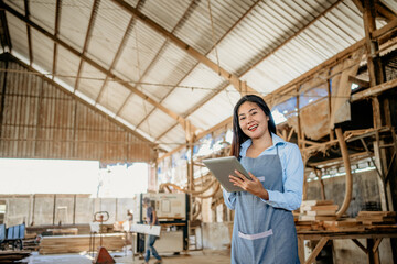 Fototapeta smiling female entrepreneur wearing an apron works with a digital tablet in a wood processing workshop obraz