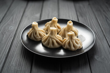 Traditional Georgian dish khinkali Kalakuri on black plate on wooden table, top view