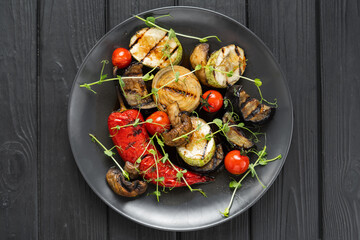 Grilled vegetables red pepper, zucchini, cherry tomatoes, mushrooms and onion on a black stone plate. Top view. Black background. Grill menu in restaurant