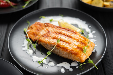 Baked grilled salmon with lemon and sauce on black background. Mediterranean diet concept.