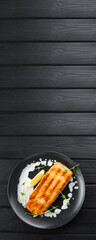 Grilled Salmon with lemon and creamy sauce on black background, vertical banner, top view, copy space.