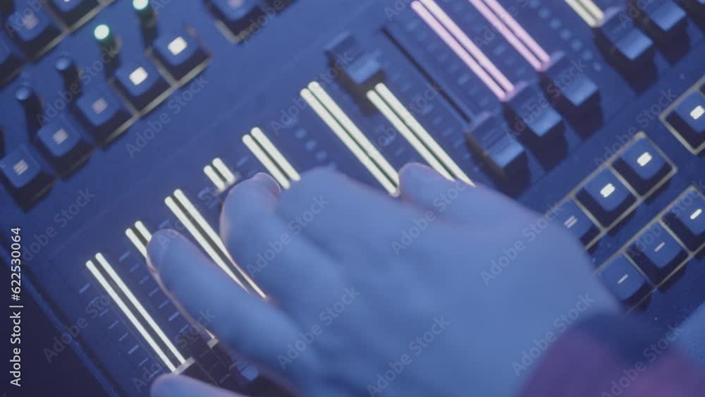 Poster male hand above an illuminated audio or light mixing panel that is sliding up and down a lit slider 