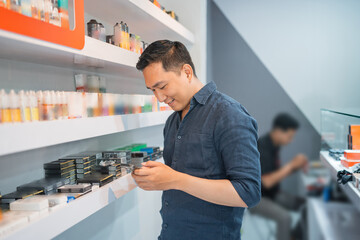 male vape seller looking at his phone while standing beside the store shelf