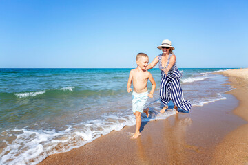 An elderly woman catches up with a boy on a sandy seashore on a sunny day. Active lifestyle, love,...
