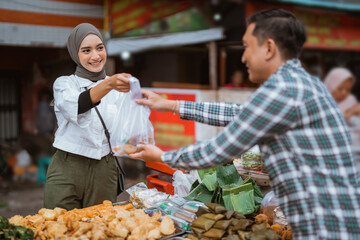 A beautiful girl wearing a headscarf selling a food stall on the side of the road gives takjil food to a buyer at the stall