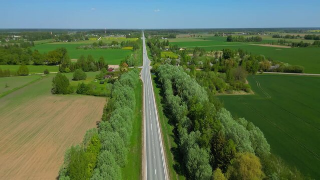 Drone reverse zoom of a rural farming community with vehicles passing through on a highway dividing the land.