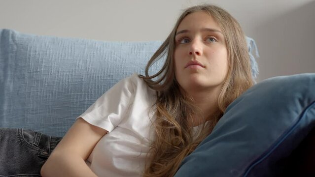 Close-up of woman using tv remote and resting head on the pillow, in Slow Motion. Girl relaxing on the sofa, watching television. 