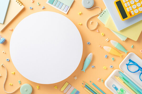 Embrace back-to-school vibe! Top-down view of stationery essentials like copybooks, pencil case, calculator, alphabet letters, sticky notes on light orange backdrop with empty circle for text or promo