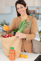 smiling young housewife with shopping bag full of vegetables