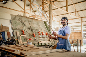 Fototapeta na wymiar male carpenter smiles at camera while holding wood material before working in wood craft workshop