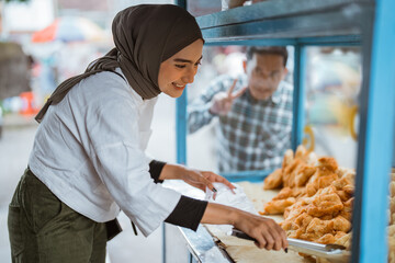 beautiful woman in hijab while sells various kinds of fried food with a cart on the side of the road