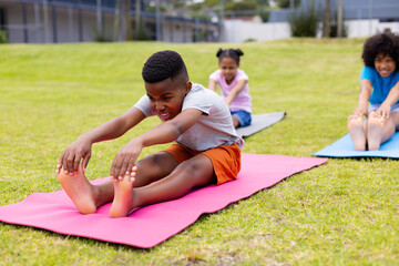 Happy african american schoolchildren doing yoga and stretching on field at school
