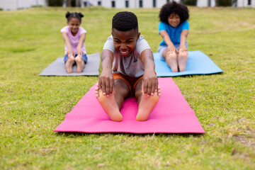 Happy african american schoolchildren doing yoga and stretching on field at school