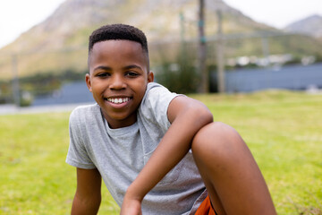 Portrait of happy african american schoolboy sitting on grass at school