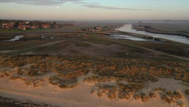 Rising flight from Walberswick beach looking towards Walberswick and Southwold harbour, Suffolk at sunrise with the moon and mist