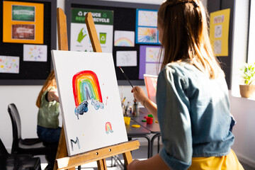 Obraz premium Happy diverse schoolchildren painting using brush and easel in school art class