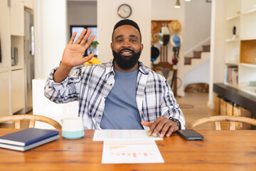 Portrait of happy african american man having video call and waving hand at home