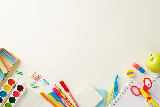 Step into the new school year with this captivating top-view image featuring notebooks, chalk and watercolor paints, colorful school supplies on a white backdrop. Customize copy-space with text or ads