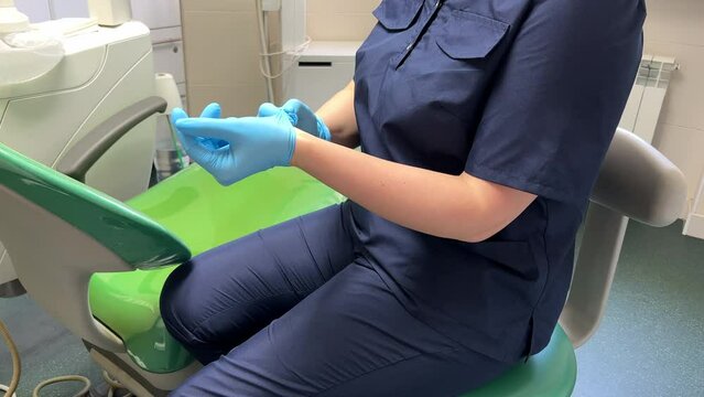Female dentist must follow the hygiene protocol before receiving a patient and puts on latex protective medical gloves. No face.