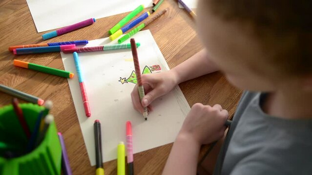 The child spends time creating and drawing. A girl draws a Christmas tree with felt-tip pens 