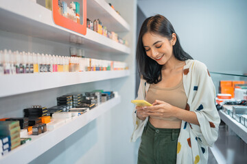 female vape seller looking at her phone while standing beside the shelf inside the vape store