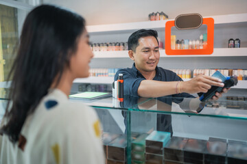 male shopkeeper helping the female customer to paying the vape stuff using the credit card