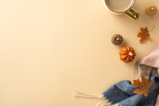 Fall coziness at home: High angle view picture of a warm patchy blanket, cup of hot cocoa, maple leaves and pumpkin candles with blank space for text or advertising on a beige isolated background