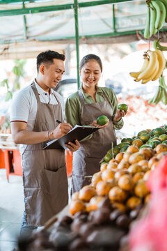 couple of asian fruit seller checking the fruits and writing on the clipboard
