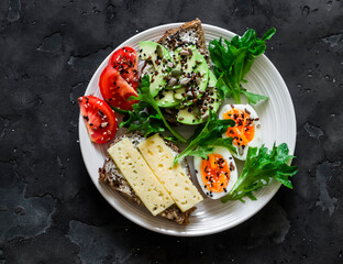 Sandwiches with avocado, cheese, seeds,  boiled egg, tomato and green salad - delicious breakfast, snack on a dark background, top view
