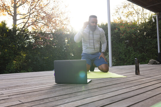 Focused african american man wearing earphones on mat with laptop in garden