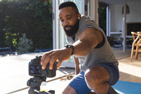 Happy african american man wearing sportswear on mat and preparing video blog at home