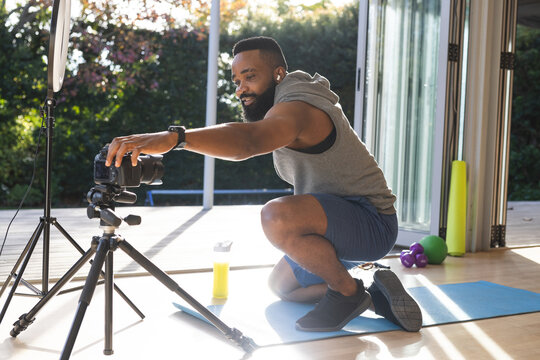 Happy african american man wearing sportswear on mat and preparing video blog at home