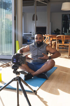 Happy african american man wearing sportswear on mat and making video blog at home
