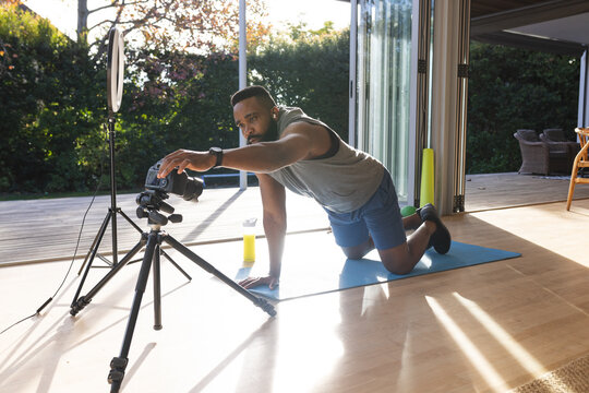 Focused african american man wearing sportswear on mat and preparing video blog at home
