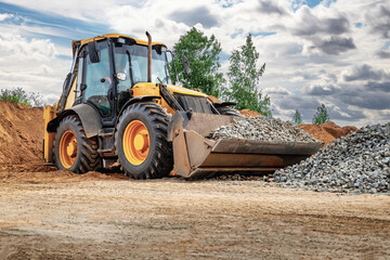 Powerful wheel loader or bulldozer against the sky. Loader transports crushed stone or gravel in a bucket. Powerful modern equipment for earthworks and bulk handling.