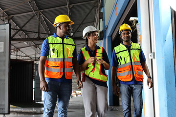 Group of warehouse workers with hardhats and reflective jackets using tablet, walkie talkie radio and cardboard while controlling stock and inventory in retail warehouse logistics, distribution center