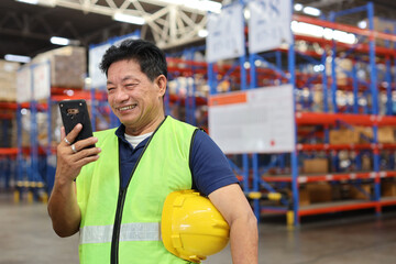 Warehouse workers man with hardhats and reflective jackets using smart mobile phone, walkie talkie radio controlling stock and inventory in retail warehouse logistics, distribution center