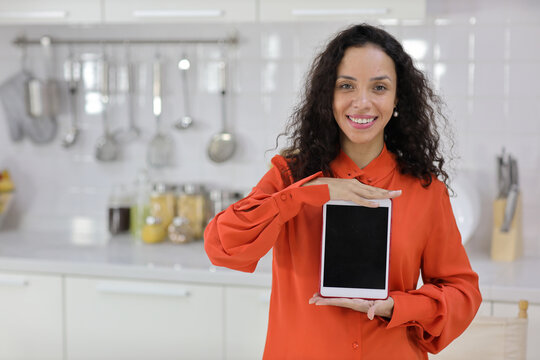 Smart and active latin woman standing while whowing tablet with happy smiling face in kitchen. Anywhere and work ifestyle with technology concept.