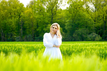 Young blond woman in white dress in cornfield. Feeling of freedom in nature.
