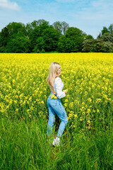 Fototapeta premium Portrait of a blond young woman in a field full of yellow flowers. Rapeseed field. Zest for life, happiness, contentment. 
