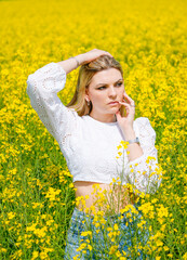Naklejka na ściany i meble Portrait of a blond young woman in a field full of yellow flowers. Rapeseed field. Zest for life, happiness, contentment. 