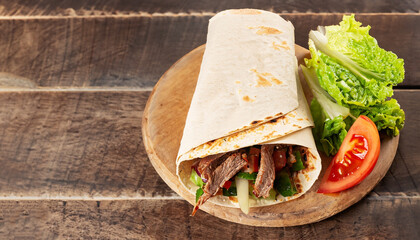 Panorama banner with spicy Turkish doner kebab filled with flaked spit roasted meat and fresh salad in a toasted tortilla wrap served on brown paper on rustic wood with copy space