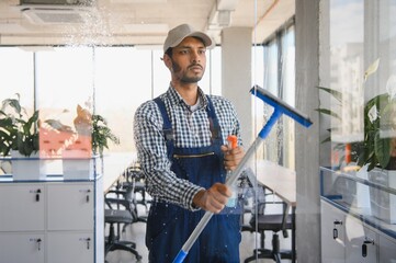 Young indian man washing window in office