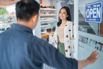beautiful female shopkeeper smiling while welcoming the male customer at front of the store