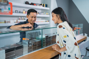 Obraz premium male shopkeeper pointing on the vape mods inside the display table while helping the female customer choosing the vape mods