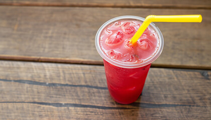 High Angle View of Refreshing and Cool Frozen Red Fruit Slush Drink in Plastic Cup Served on Rustic Wooden Table with Bright Yellow Straw and Copy Space