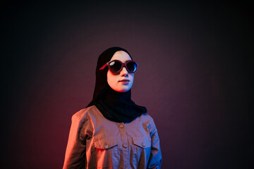 muslim woman wearing black hijab orange long dress and sunglasses posing sideways
