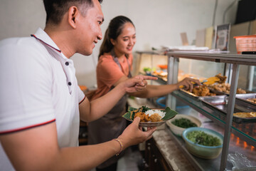 closeup of a handsome man choosing food with pointing finger with a female waitress at a traditional stall