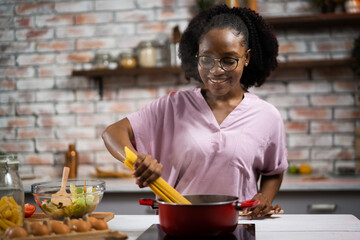 Fototapeta na wymiar Young woman in kitchen. Beautiful African woman cooking pasta.